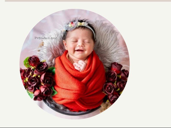Smiling newborn wrapped in red fabric surrounded by roses